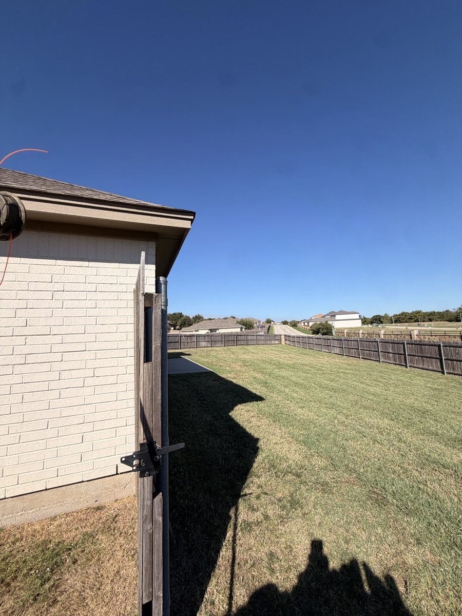 Mowed side lawn beside a house and fence in Weatherford, Texas.
