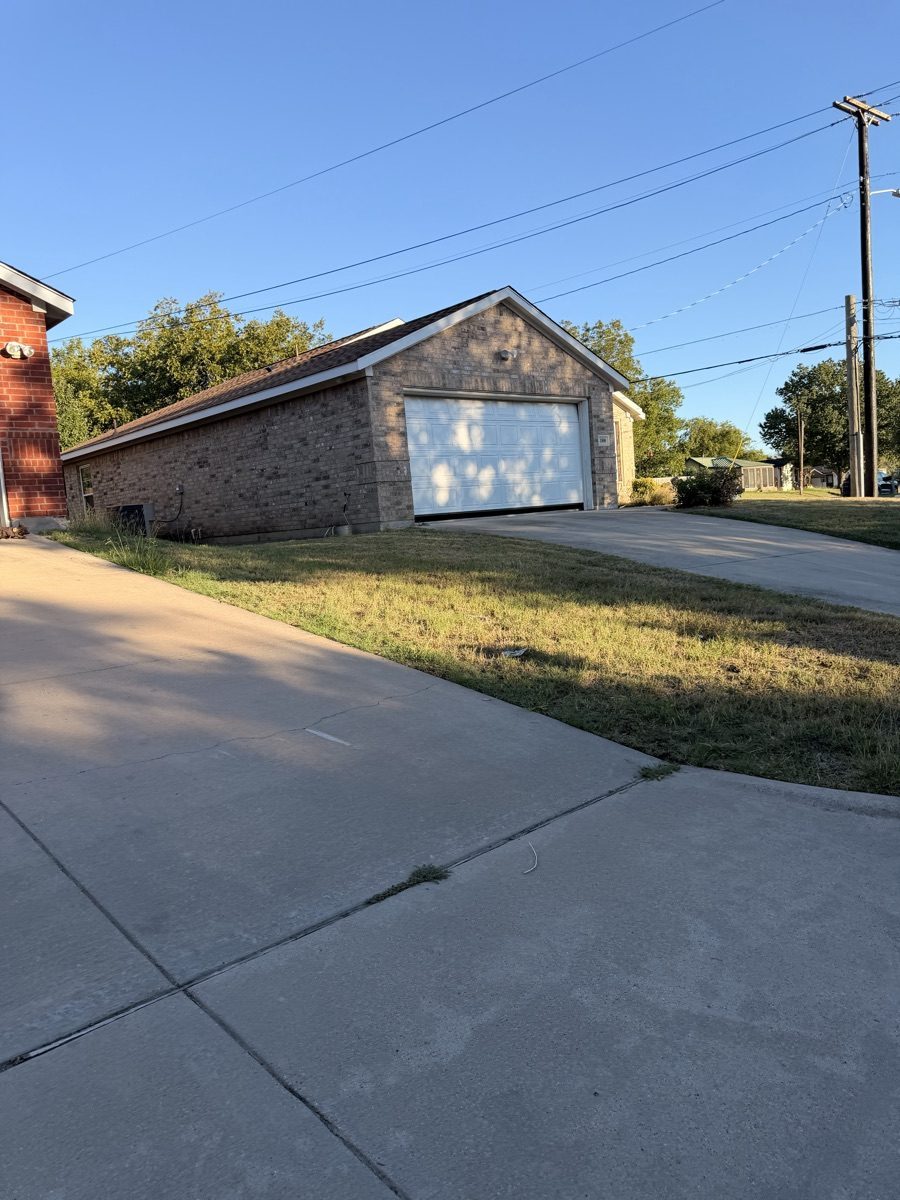 Grass beside a brick garage and driveway before mowing in Weatherford, Texas.