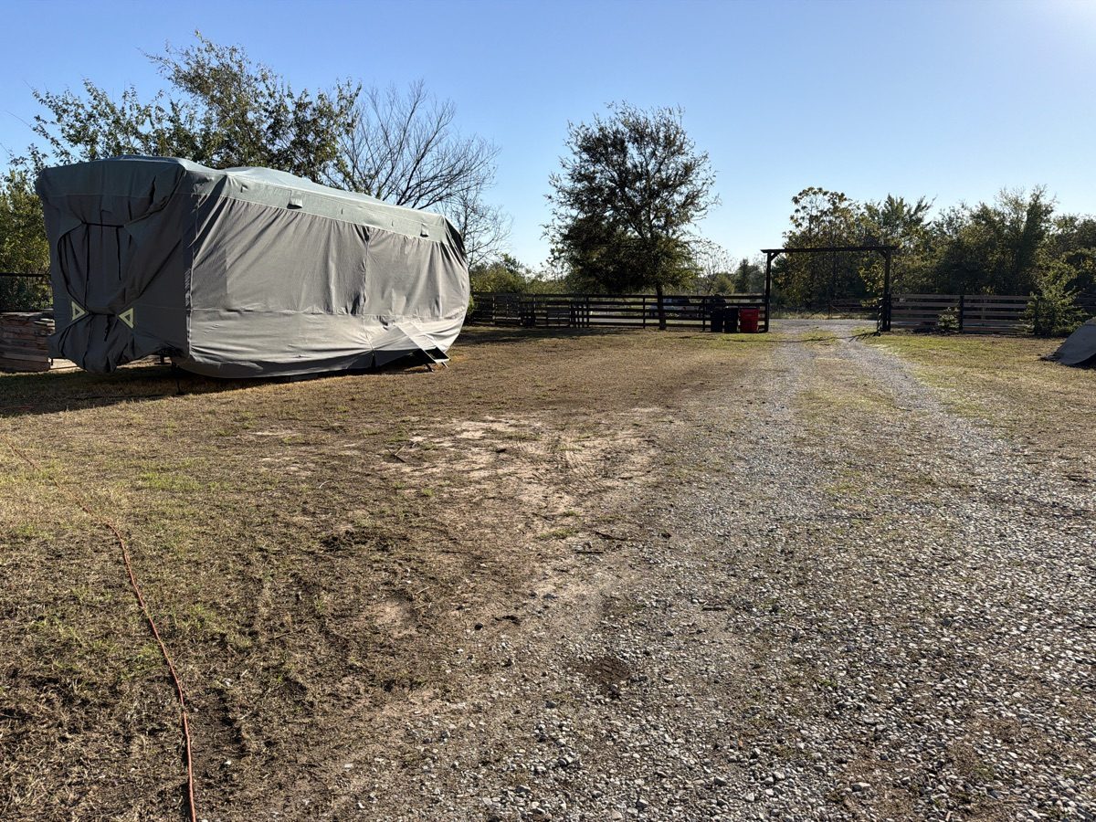 Mowed grass alongside a gravel driveway, covered trailer, and fence in Azle, Texas.